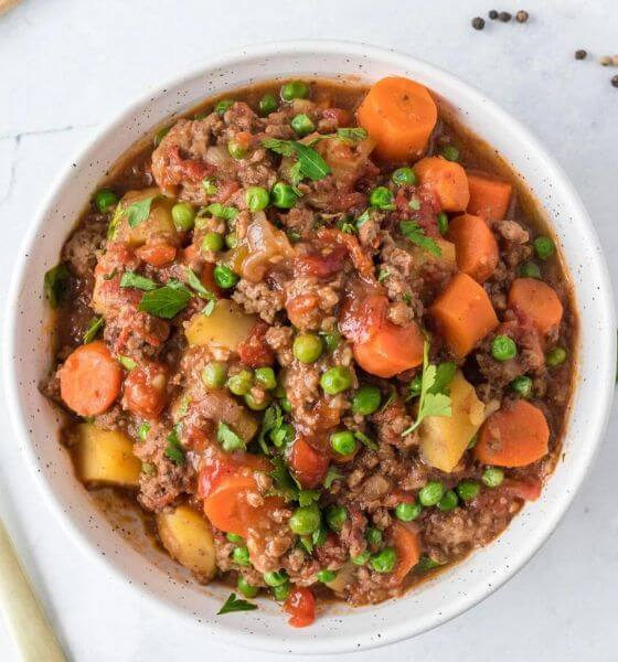 Hamburger stew in white bowl with carrots and peas