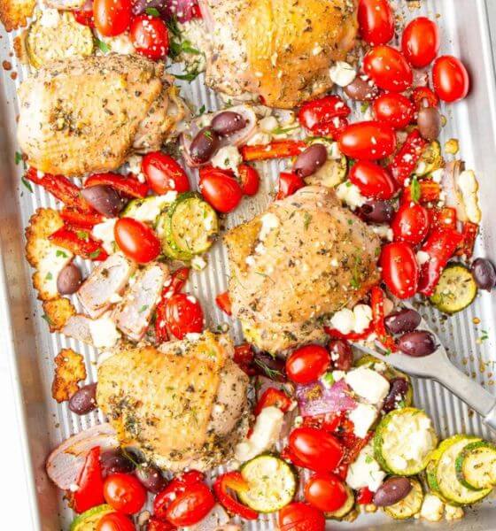 Chicken with tomatoes, olives, onions and cheese on a baking sheet