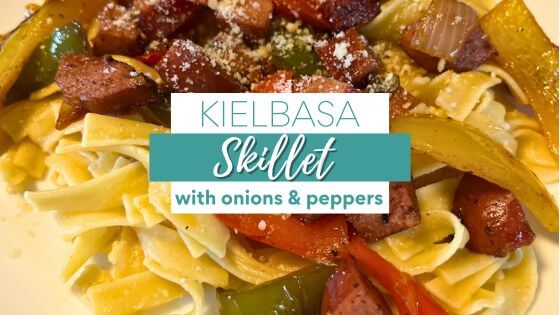 Kielbasa with onions and peppers over noodles on white plate