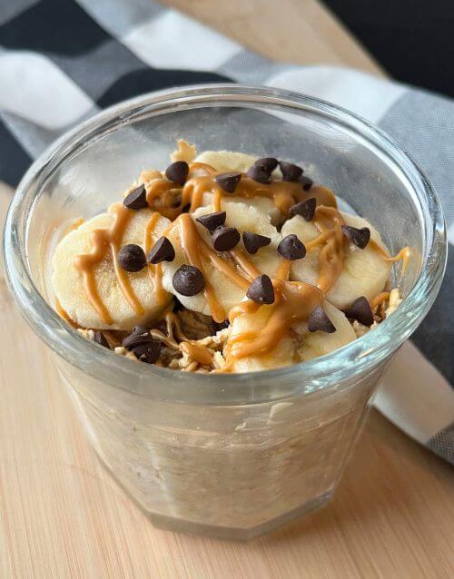 overnight oats in glass jar with banana slices and peanut butter and chocolate chips on top